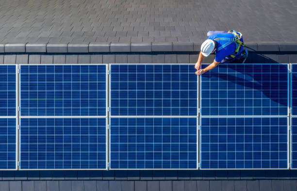 Male engineer in blue suit and protective helmet installing photovoltaic panel system. Professional electrician mounting solar module on roof. Alternative energy ecological concept