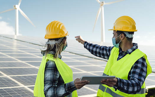 People working for alternative energy with wind turbine and solar panel while wearing face mask during corona virus outbreak - Innovation and green power concept