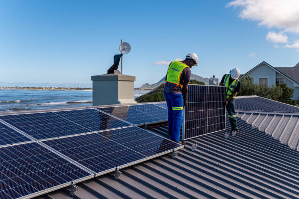 Two African men install solar panels neatly on a residential roof of a house near the ocean. Sustainable living.
